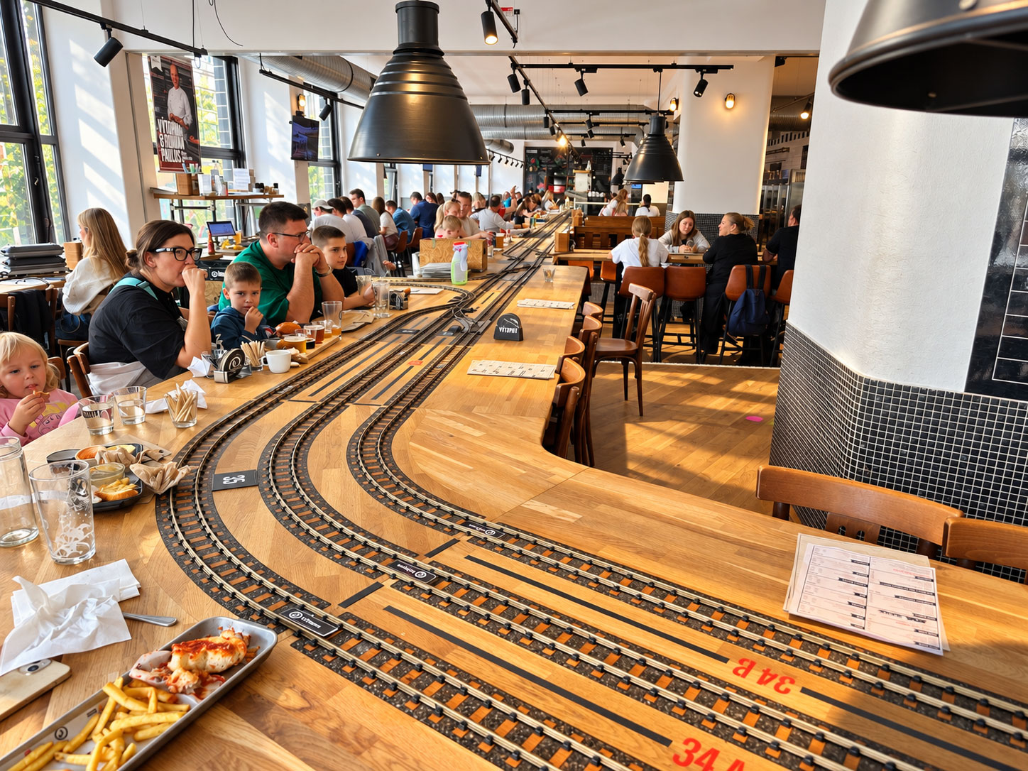 Gäste an Tischen mit Modelleisenbahnschienen im Výtopna Railway Restaurant Prag